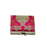 A small rectangular fabric pouch or clutch with a bright pink background and ornate silver, gold, and pale blue floral and scrollwork pattern, shown closed on a light gray studio background.